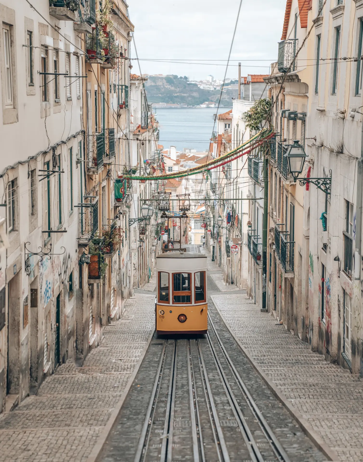 Lisbon — a yellow funicular tram climbing a narrow street with the Tagus river in the distance